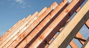 Wooden roof trusses of a building under construction against a clear blue sky.