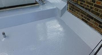 Flat roof section with a fresh coat of white waterproof sealing adjacent to a brick wall.